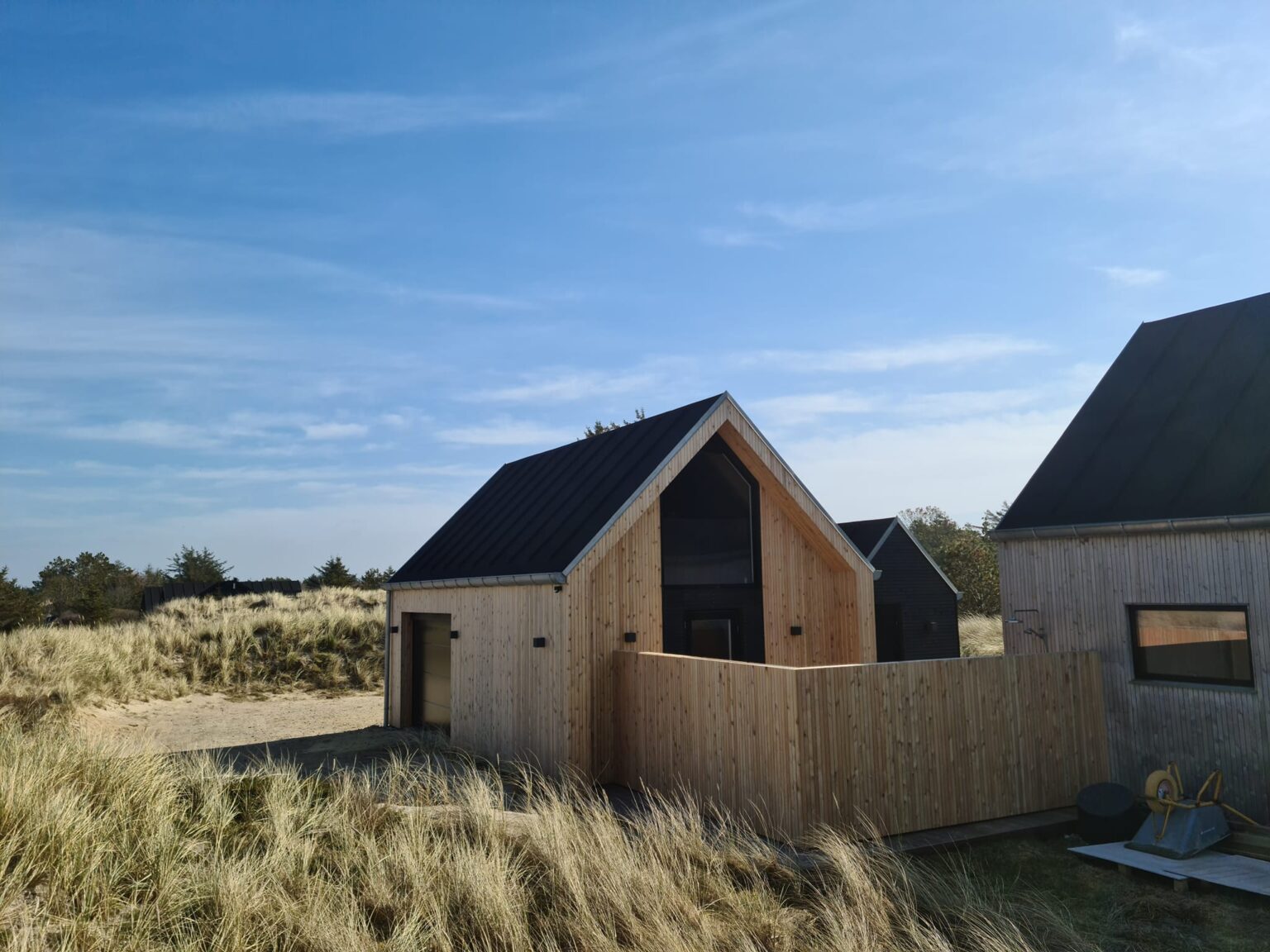 Moderne træsommerhus ved klitter og blå himmel