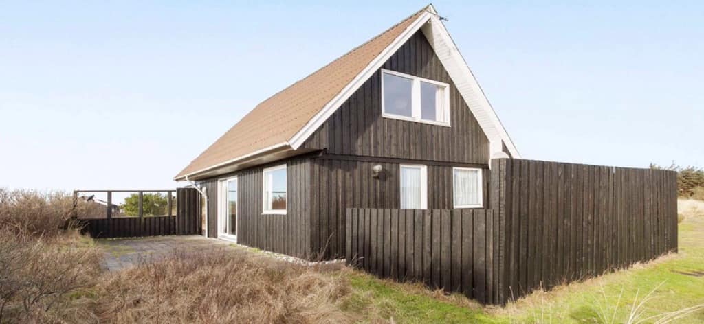 Sort sommerhus med skrå tag nær klitterne